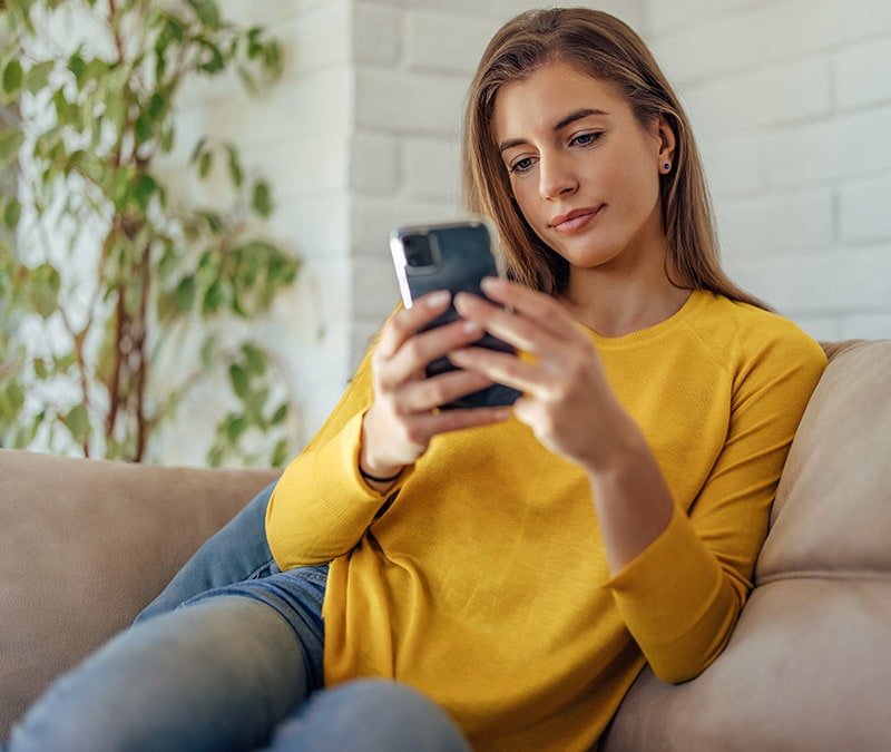 Une femme assise sur un canapé avec un smartphone, découvrant comment supprimer un compte Instagram