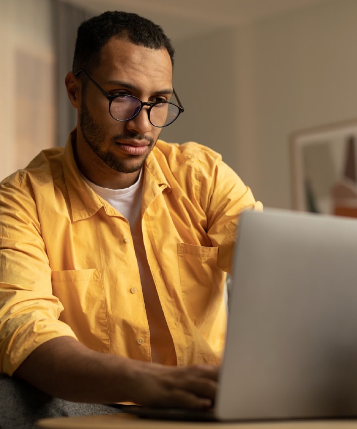 Un homme portant une chemise jaune qui regarde son ordinateur portable qui peut être infecté par un spyware.