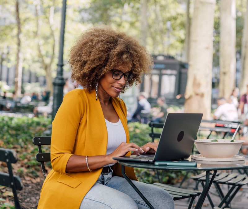 Une femme utilise un VPN pour préserver la confidentialité des données de son entreprise lorsqu'elle travaille depuis une terrasse.