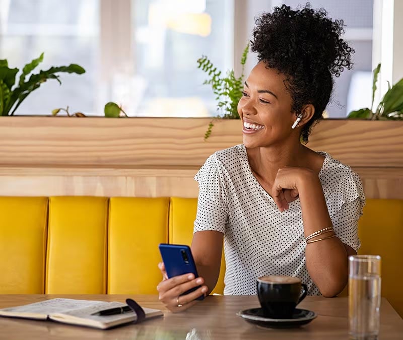 Une femme souriante sur son iPhone dans un café après avoir appris à utiliser un VPN sur un iPhone pour rester en sécurité.