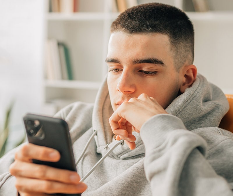Un jeune homme vêtu d'un sweat à capuche gris étudie attentivement son iPhone, à la recherche d'informations sur ce que sont les virus d'iPhone et sur la manière de s'en débarrasser.