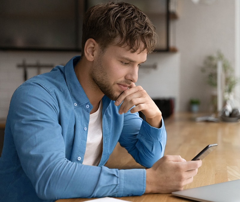 Personne à l'expression confuse regardant son téléphone, se demandant potentiellement « Comment savoir si un numéro m'a bloqué ? »