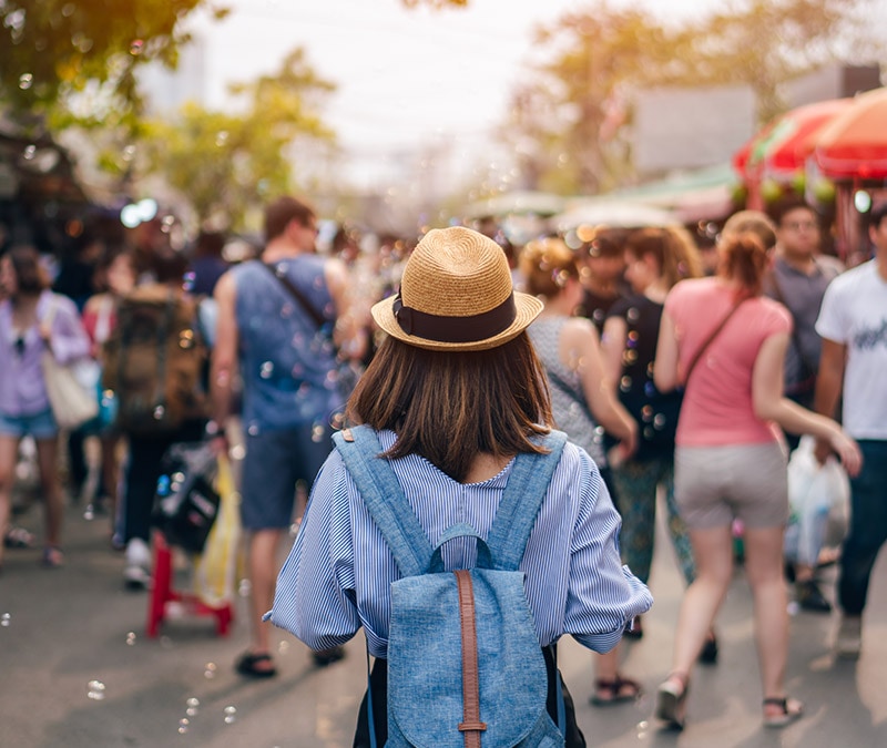 Une femme portant un chapeau de paille et un sac à dos parcourt un marché en plein air très fréquenté, symbolisant la prudence à l'égard des escroqueries sur Facebook Marketplace.