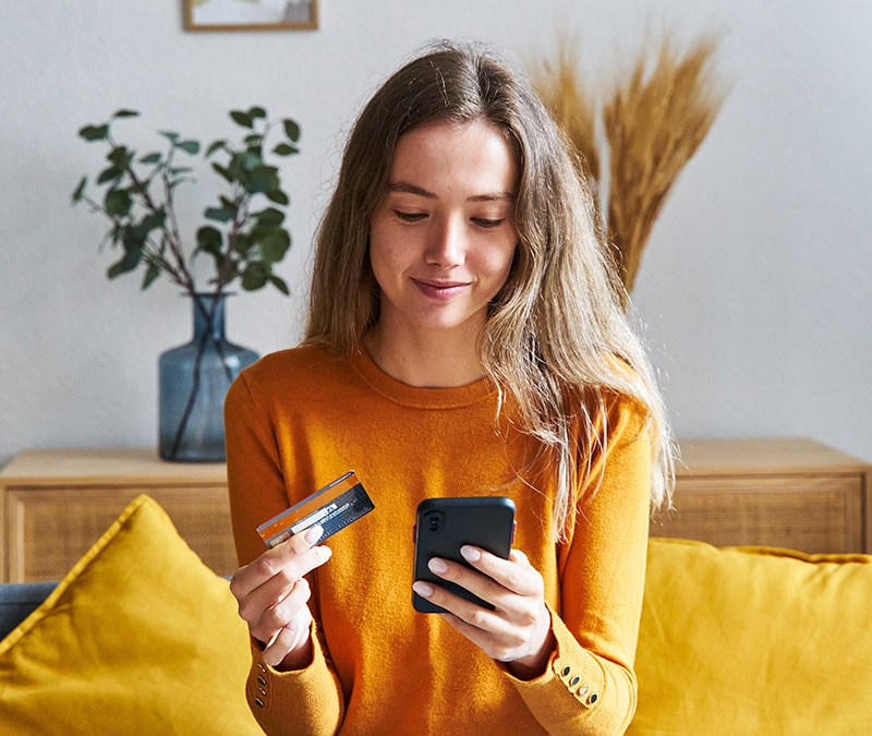 Une jeune femme tenant une carte de crédit et un smartphone, réfléchissant à la manière de supprimer son empreinte numérique lors de ses achats en ligne.
