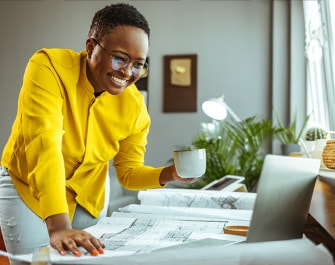 Une femme souriante qui tient une tasse et regarde un ordinateur portable